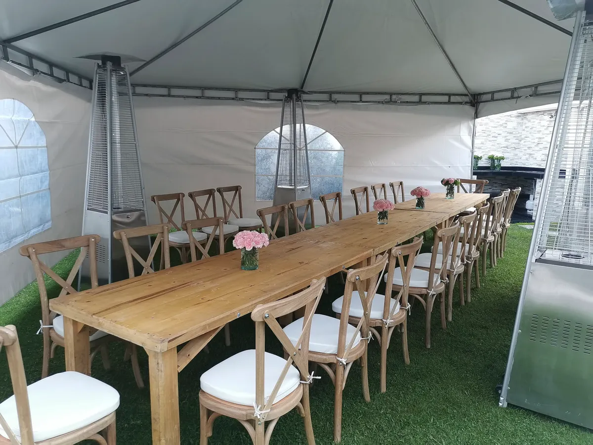 Montaje de boda al aire libre con mesa larga en madera y sillas cross-back bajo carpa
